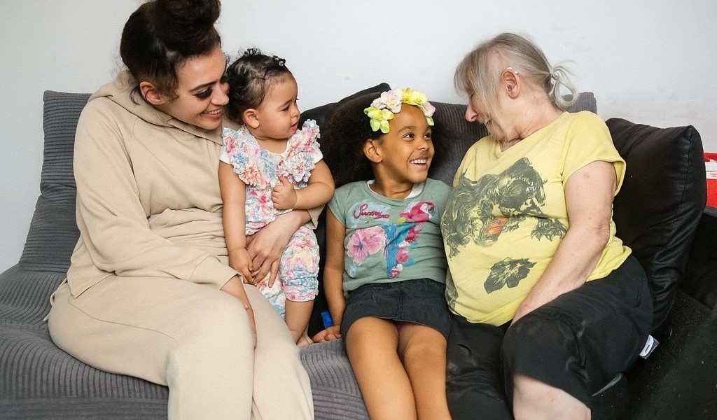 Grandmother, mother and two children sitting smiling on a sofa.