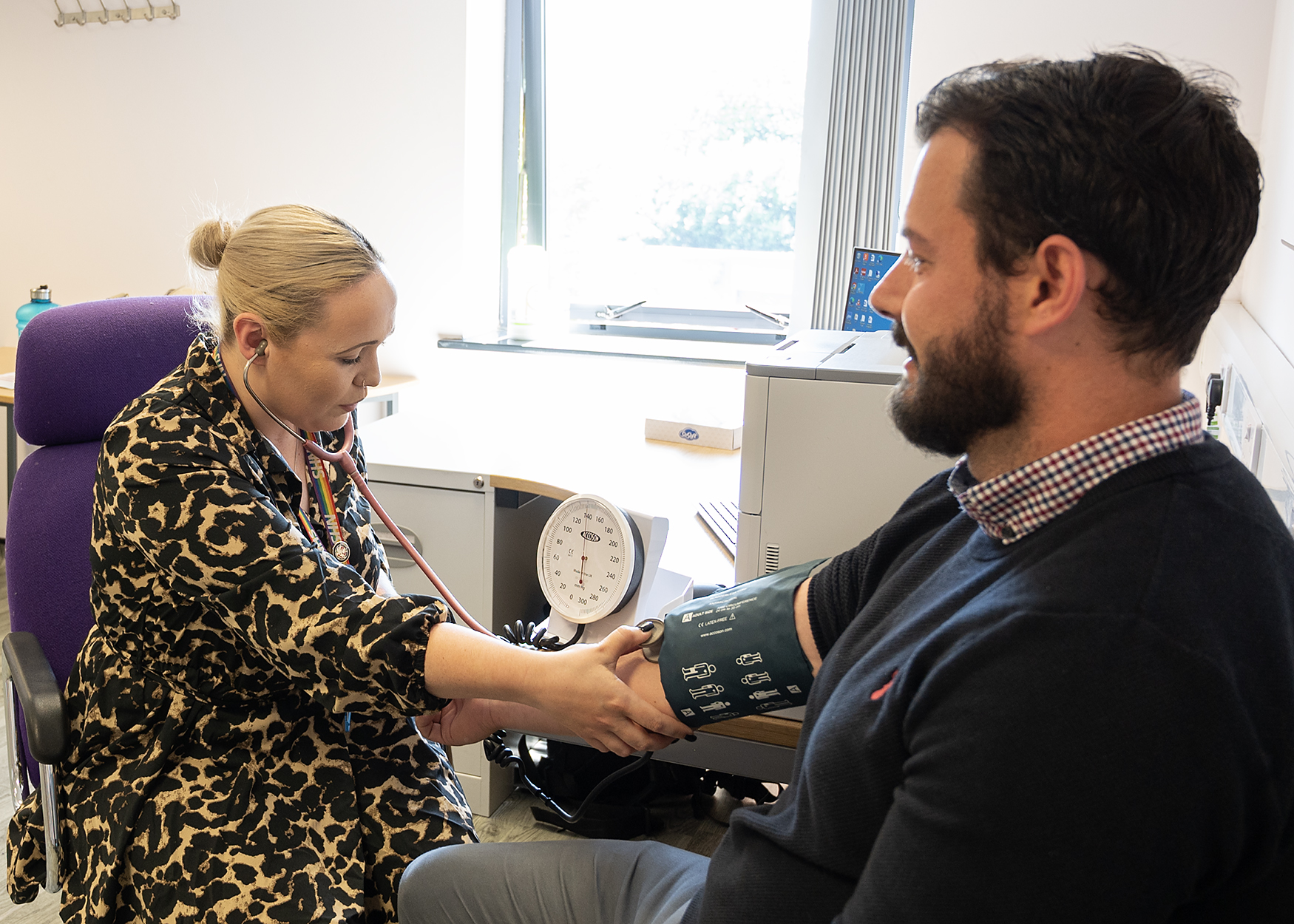 GP writing notes and taking a patient's blood pressure.